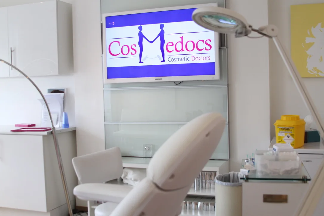 Cosmedocs original treatment room with a single medical chair, magnifying lamp and wall-mounted brand screen