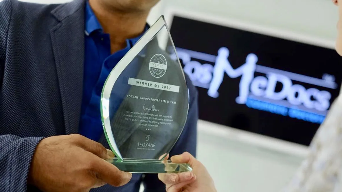 Teoxane Laboratories Outstanding Clinical Award trophy presented to Cosmedocs in 2017, in front of the CosmeDocs Cosmetic Doctors logo