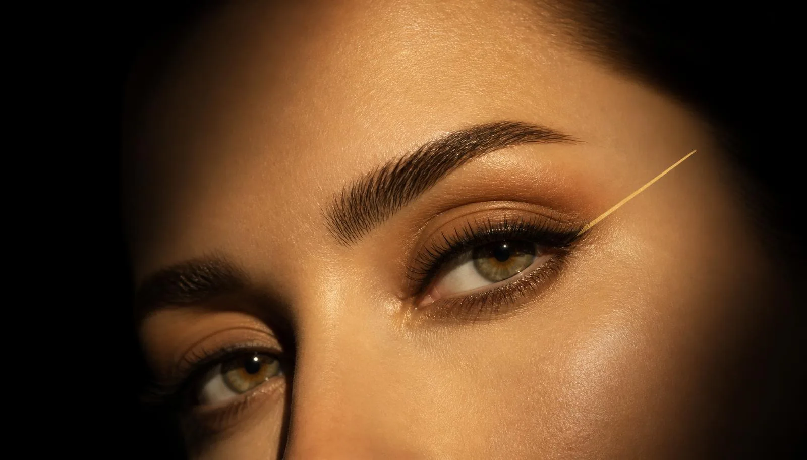 Gold line-art diagram of two eyes with an axis line through the inner and outer corners illustrating canthal tilt