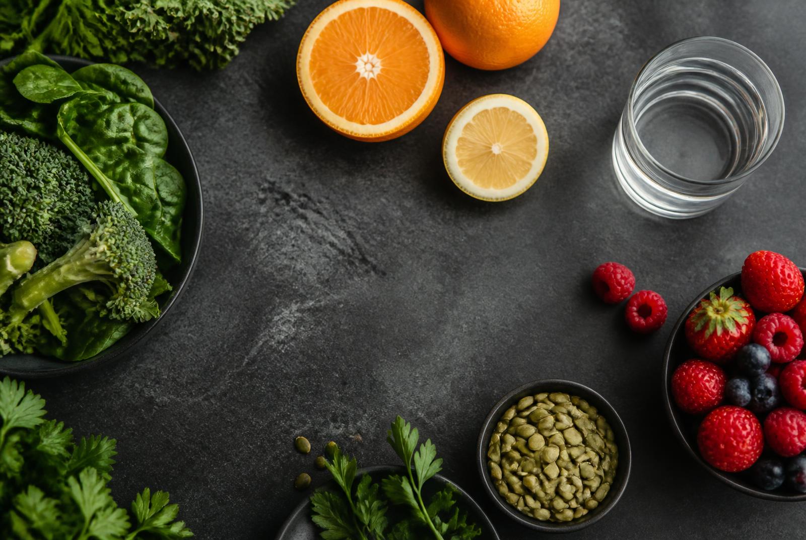 Citrus fruit, berries, leafy greens and seeds arranged on dark stone